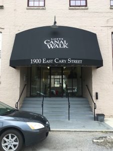Sophisticated black-fabric awning with Canal Walk and street address graphics over steps leading up to double glass doors on a beige brick buildingon