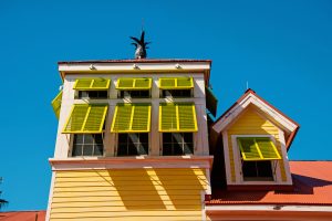 Yellow aluminun Bahama shutters of multiple sizes on second story windows of a building with a terracotta roof